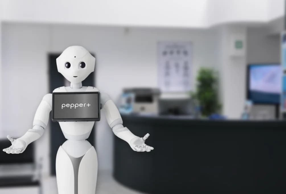 The Pepper+ robot at a reception desk, with its arms open
