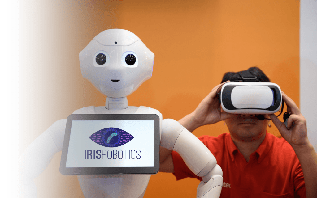 Robotul Pepper cu sigla IRIS Robotics pe tabletă, lângă un bărbat cu ochelari VR
